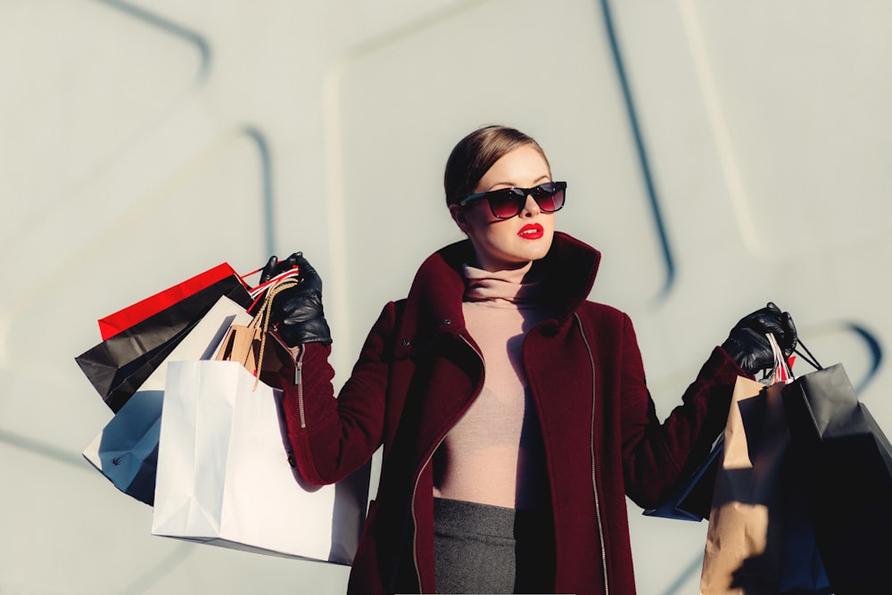 A woman in a tailored coat carrying shopping bags, representing curated fashion and lifestyle privileges