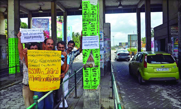 Local people and motorists sticking posters announcing withdrawal of toll collection at Aroor toll booth on Sunday. (Photo: DC) Local people and motorists sticking posters announcing withdrawal of toll collection at Aroor toll booth on Sunday. (Photo: DC)