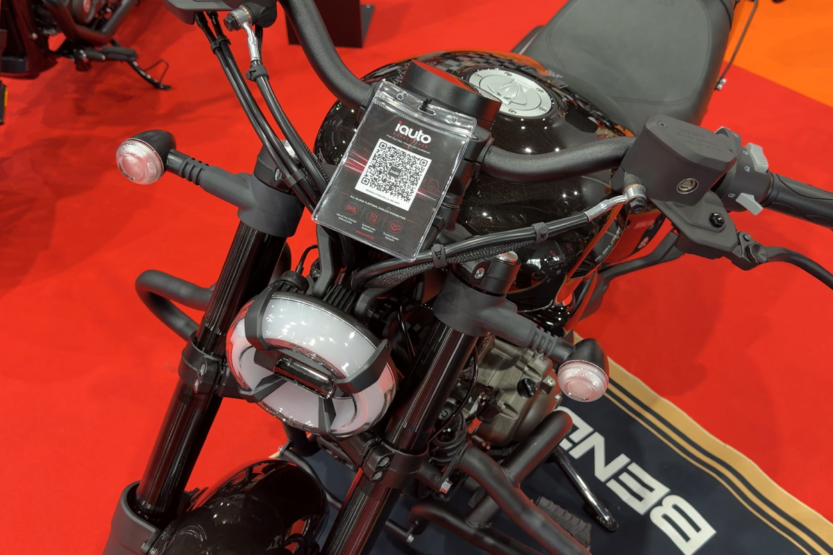 A close-up view of a Benelli motorcycle's round headlight and handlebars, highlighting a clear acrylic scannable iauto.sg QR code display panel mounted in the center.