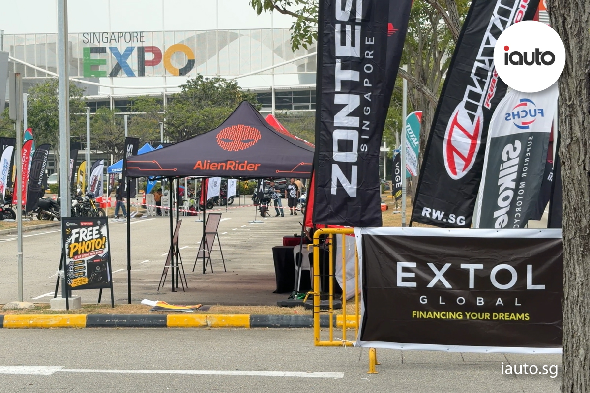 An outdoor event space at Singapore EXPO featuring promotional tents and tall flags for motorcycle brands and finance providers like Extol Global.