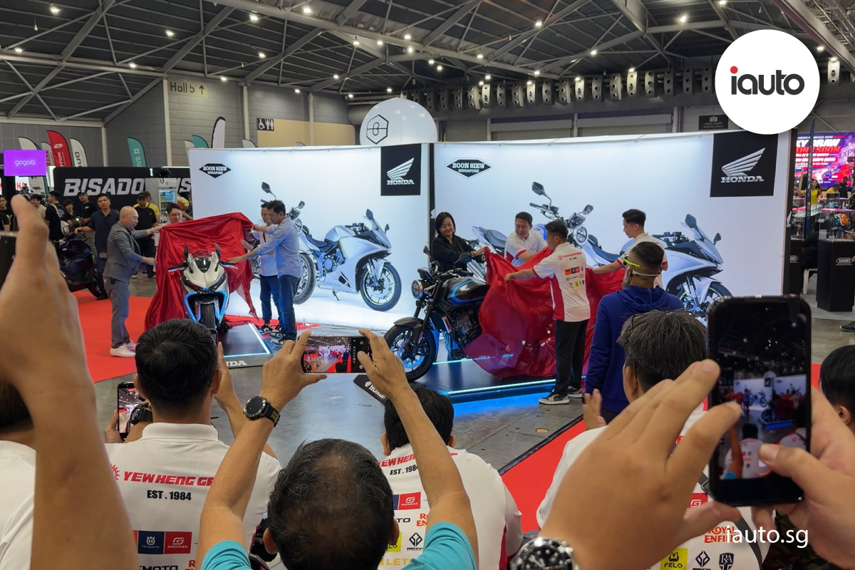 A crowd of attendees raising their smartphones to capture photos as executives unveil new Honda motorcycles from underneath red cloths.