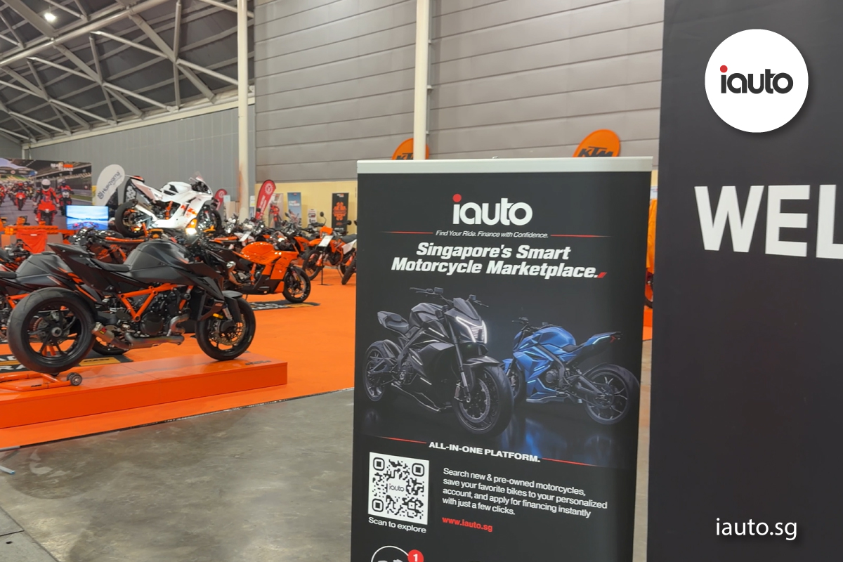 A vertical banner graphic for iAuto Marketplace positioned next to a large "WELCOME" sign and a display of orange KTM motorcycles.