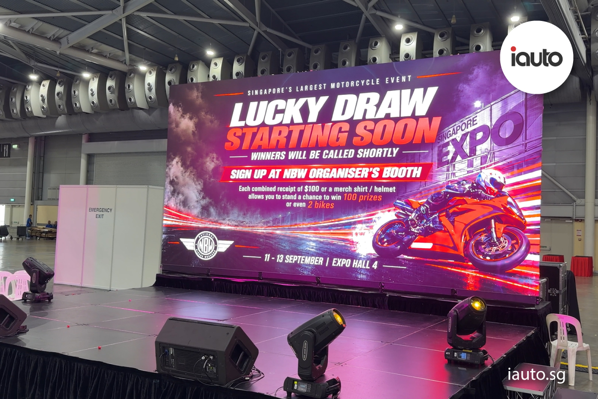 A large brightly lit LED stage screen at Singapore EXPO displaying a "Lucky Draw Starting Soon" announcement for the National Bikers Weekend event.
