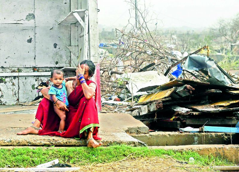 A woman sits with her child next to storm-damaged buildings in Puri, Odisha