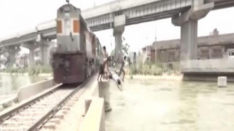 Whenever a train approaches, these children climb railways track and jump into a nearby canal, throwing caution out of the window. (Photo: ANI)