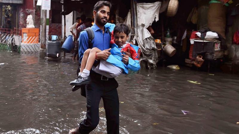 A man, holding a school boy, walks through a waterlogged street in Kolkata on Thursday after rains. (Photo: PTI)
