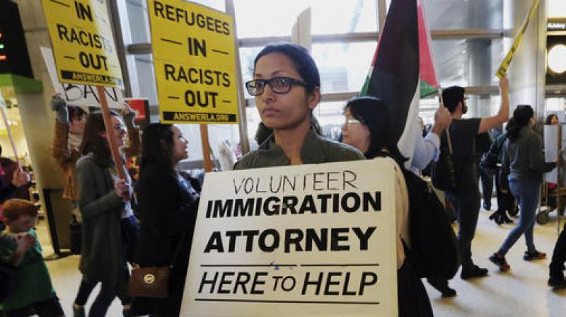 A woman offers legal services at the customs arrival area as demonstrators opposed to President Donald Trump's executive orders barring entry to the US by Muslims from certain countries march behind at the Tom Bradley International Terminal at Los Angeles International Airport. (Photo: AP) A woman offers legal services at the customs arrival area as demonstrators opposed to President Donald Trump's executive orders barring entry to the US by Muslims from certain countries march behind at the Tom Bradley International Terminal at Los Angeles International Airport. (Photo: AP)
