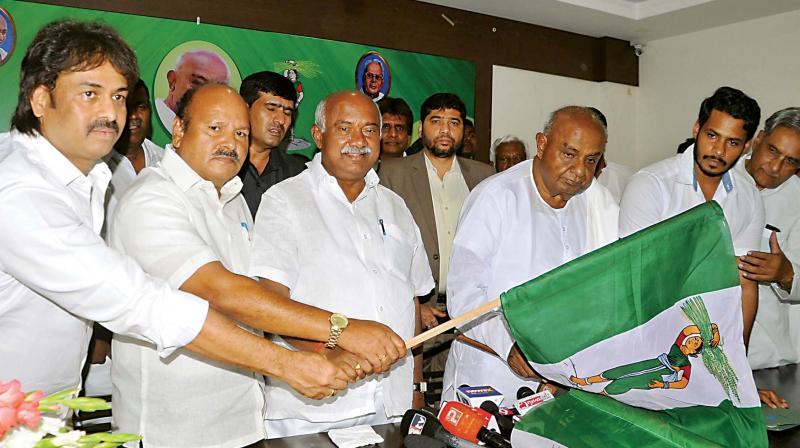 Outgoing state JD(S) chief A.H. Vishwanath and party supremo H.D. Deve Gowda present the JD(S) flag to newly chosen state unit chief H.K. Kumaraswamy in Bengaluru on Thursday. (Photo: DC) Outgoing state JD(S) chief A.H. Vishwanath and party supremo H.D. Deve Gowda present the JD(S) flag to newly chosen state unit chief H.K. Kumaraswamy in Bengaluru on Thursday. (Photo: DC)