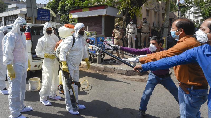 Media personnel maintain social distance as they interview, using modified mics, health workers sanitising an area near Nizamuddin mosque, Delhi. PTI Photo