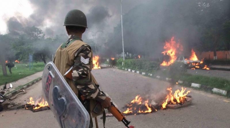 A Security personnel stands towards vehicles burning in violence following Dera Sacha Sauda chief Gurmeet Ram Rahim’s conviction in Panchkula on Friday. (Photo: PTI) A Security personnel stands towards vehicles burning in violence following Dera Sacha Sauda chief Gurmeet Ram Rahim’s conviction in Panchkula on Friday. (Photo: PTI)