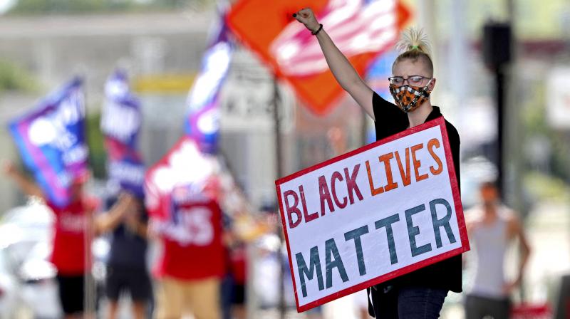 A Black Lives Matter protester salutes passing traffic while supporters of President Donald Trump rally in the background. (AP)