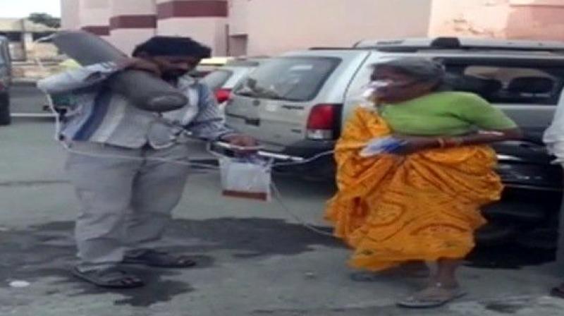 A picture of a man carrying an oxygen cylinder attached to his ailing mother, on his shoulder, has gone viral on social media. (Photo: ANI | Twitter) A picture of a man carrying an oxygen cylinder attached to his ailing mother, on his shoulder, has gone viral on social media. (Photo: ANI | Twitter)