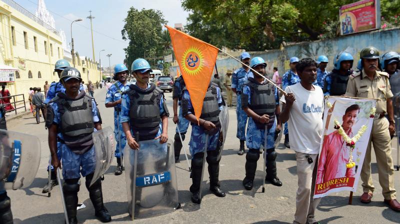A protester carries the poster of RSS worker Rudresh,who was murdered yesterday as Rapid Action Force personnel stand guard in Shaivajinagar area during a protest rally against the murder of RSS worker in Bengaluru. (Photo: PTI) A protester carries the poster of RSS worker Rudresh,who was murdered yesterday as Rapid Action Force personnel stand guard in Shaivajinagar area during a protest rally against the murder of RSS worker in Bengaluru. (Photo: PTI)