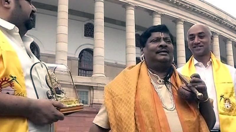 Dressed as Annamayya, Sivaprasad was seen with a gold silk drape around his shoulders, a yellow waist band and was seen holding an iktara, near the Mahatma Gandhi statue in the parliament complex. (Photo: ANI) Dressed as Annamayya, Sivaprasad was seen with a gold silk drape around his shoulders, a yellow waist band and was seen holding an iktara, near the Mahatma Gandhi statue in the parliament complex. (Photo: ANI)