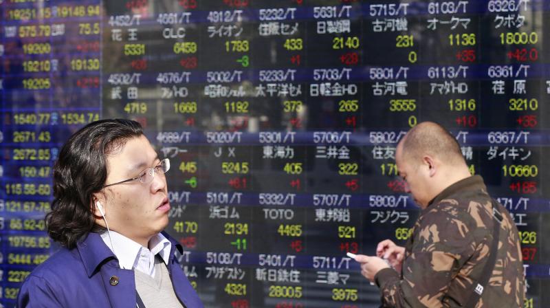 People walk past an electronic stock indicator of a securities firm in Tokyo. (Photo:AP) People walk past an electronic stock indicator of a securities firm in Tokyo. (Photo:AP)
