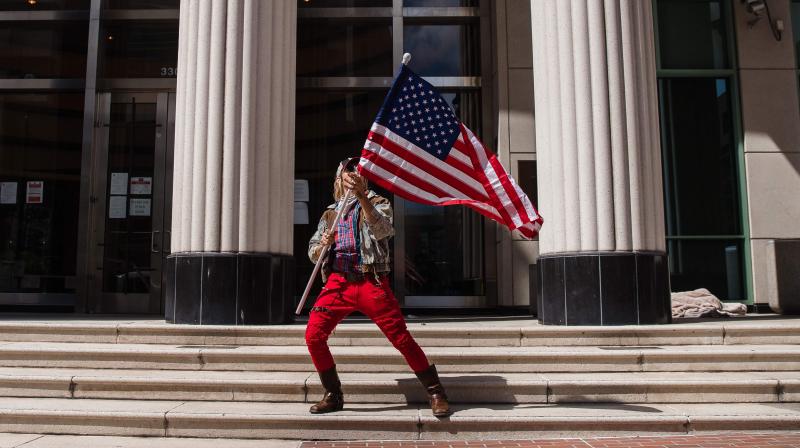 A man waves the US flag in front of the Hall of Justice Courthouse while protesters rally in downtown San Diego against Californias stay at home order to prevent the spread of the novel coronavirus, which causes COVID-19, on Saturday. (AFP)