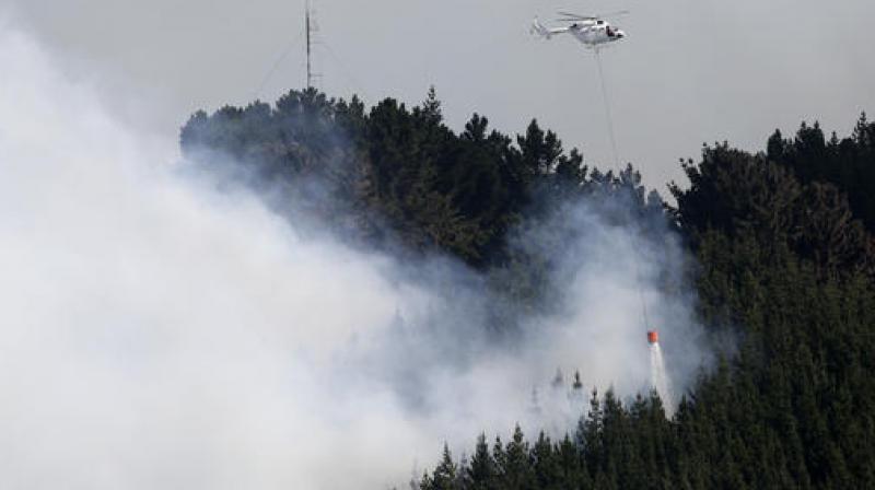A helicopter dumps water on a wild fire in the Port Hills near Christchurch. (Photo: AP) A helicopter dumps water on a wild fire in the Port Hills near Christchurch. (Photo: AP)