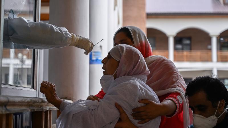 Relatives hold an elderly woman (C) as a health worker takes a nasal swab sample to test for the COVID-19 coronavirus at a testing centre in Srinagar. AFP Photo