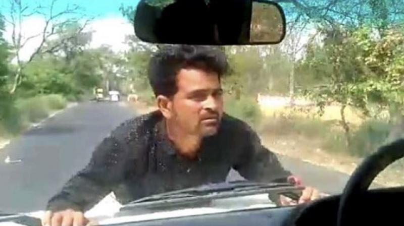 A man clings on to the bonnet of a car in UP's Ramnagar as a block development officer drives for 4 km. (YouTube | Screengrab) A man clings on to the bonnet of a car in UP's Ramnagar as a block development officer drives for 4 km. (YouTube | Screengrab)