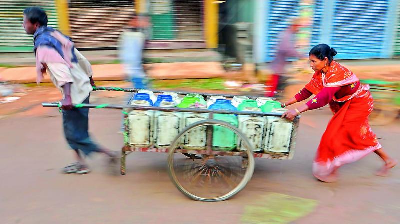 Labourers carry tins of drinking water for distribution to food stalls in Agartala on Tuesday. (Photo: AFP) Labourers carry tins of drinking water for distribution to food stalls in Agartala on Tuesday. (Photo: AFP)