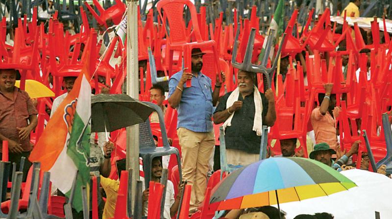 Supporters of JD(S) and Congress use chairs to protect themselves from rain during the swearing-in ceremony in Bengaluru on Wednesday. (Photo:DC) Supporters of JD(S) and Congress use chairs to protect themselves from rain during the swearing-in ceremony in Bengaluru on Wednesday. (Photo:DC)