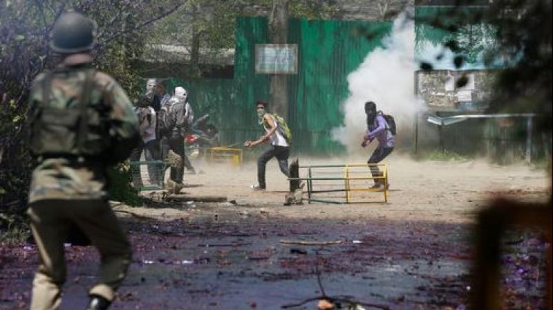 Kashmiri students throw stones on Indian policemen as tear smoke shell explodes near them. (Photo: PTI) Kashmiri students throw stones on Indian policemen as tear smoke shell explodes near them. (Photo: PTI)