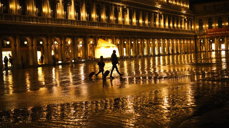 Tourists pull their luggage as they walk through a nearly empty St. Mark's Square on a rainy day in Venice. The coronavirus outbreak in northern Italy has so overwhelmed the public health system that officials are taking extraordinary measures to care for the sick, seeking to bring doctors out of retirement and accelerate graduation dates for nursing students. (AP) Tourists pull their luggage as they walk through a nearly empty St. Mark's Square on a rainy day in Venice. The coronavirus outbreak in northern Italy has so overwhelmed the public health system that officials are taking extraordinary measures to care for the sick, seeking to bring doctors out of retirement and accelerate graduation dates for nursing students. (AP)