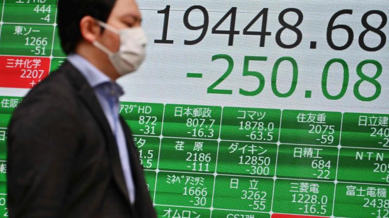 A mask-clad pedestrian passes in front of a quotation board displaying the share price numbers of the Tokyo Stock Exchange in Tokyo on march 10, 2020(AFP)