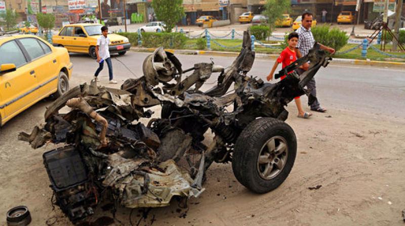 Civilians pass a destroyed car in the a car bomb explosion in southwestern Baghdad, Iraq. (Photo: AP) Civilians pass a destroyed car in the a car bomb explosion in southwestern Baghdad, Iraq. (Photo: AP)