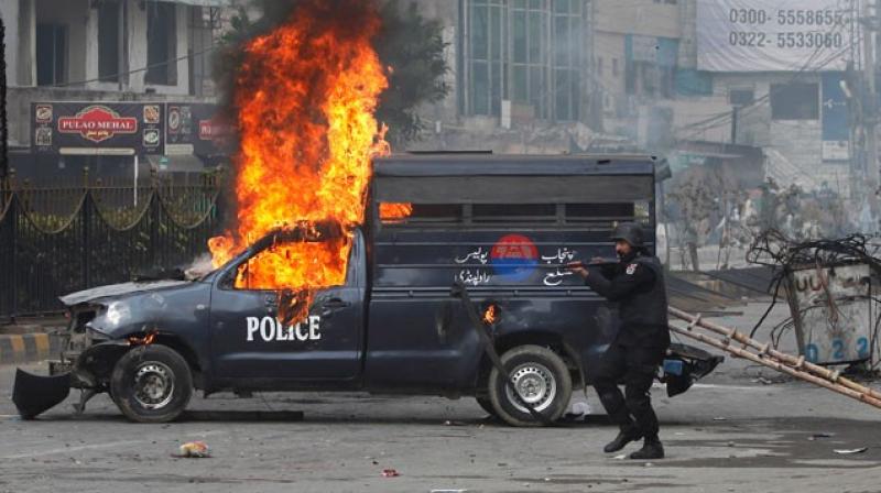 A Pakistani police officer aims his gun towards the protesters next to a burning police vehicle during a clash in Islamabad, Pakistan. (Photo: AP) A Pakistani police officer aims his gun towards the protesters next to a burning police vehicle during a clash in Islamabad, Pakistan. (Photo: AP)