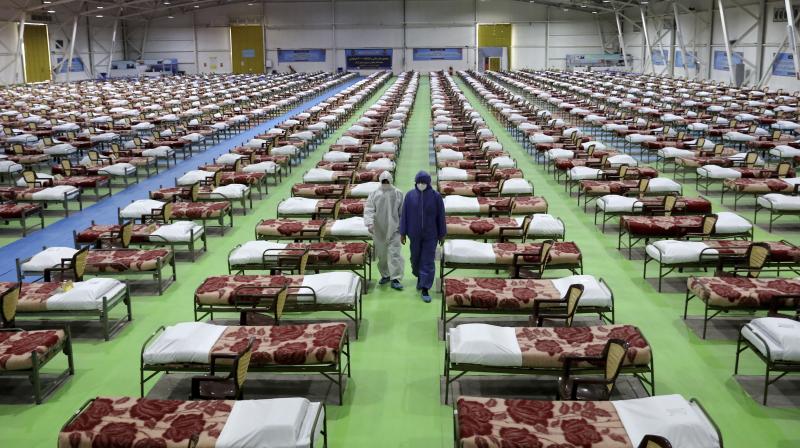 People in protective clothing walk past rows of beds at a temporary 2,000-bed hospital for COVID-19 coronavirus patients set up by the Iranian army at the international exhibition center in northern Tehran, Iran. AP Photo