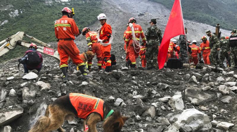 Rescuers with sniffer dogs stand near earth moving equipment digging at the site of a landslide in Xinmo village in Maoxian County in southwestern China (Photo: AP) Rescuers with sniffer dogs stand near earth moving equipment digging at the site of a landslide in Xinmo village in Maoxian County in southwestern China (Photo: AP)