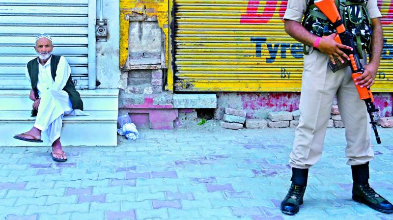An elderly man sits as Indian paramilitary trooper stands guard in front of closed shops during a lockdown in Srinagar on Monday. (AFP) An elderly man sits as Indian paramilitary trooper stands guard in front of closed shops during a lockdown in Srinagar on Monday. (AFP)