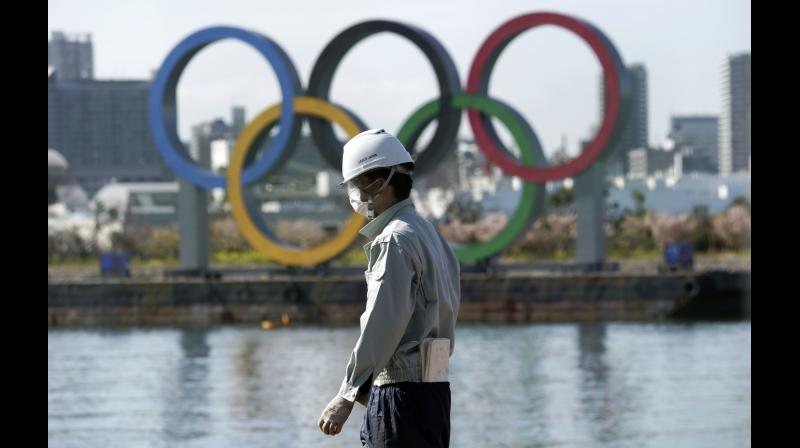 A masked man works at a construction site with the Olympic rings in the background on Tuesday. AP Photo