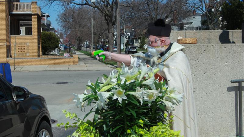 Rev. Timothy Pelc blesses Easter baskets outside St. Ambrose Church in Grosse Pointe Park. He offered a prayer and sprayed holy water from a squirt gun instead of blessing baskets inside the church in a bid to maintain social distancing during the coronavirus pandemic. (AP) Rev. Timothy Pelc blesses Easter baskets outside St. Ambrose Church in Grosse Pointe Park. He offered a prayer and sprayed holy water from a squirt gun instead of blessing baskets inside the church in a bid to maintain social distancing during the coronavirus pandemic. (AP)