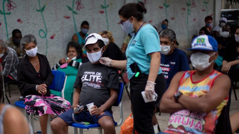 A caretaker fix the face mask of a resident of the public shelter Stella Maris as they wait seated respecting social distance while Brazils Armed Forces soldiers disinfect the place. (AFP)