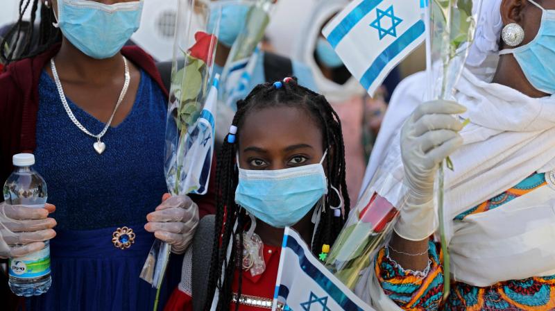 Ethiopian Jewish immigrants making their Aliyah (Immigration to Israel) in protective gear amid the COVID-19 pandemic, wave Israeli flags as they step off a plane at Ben Gurion International Airport in Lod, east of Tel Aviv. (AFP)