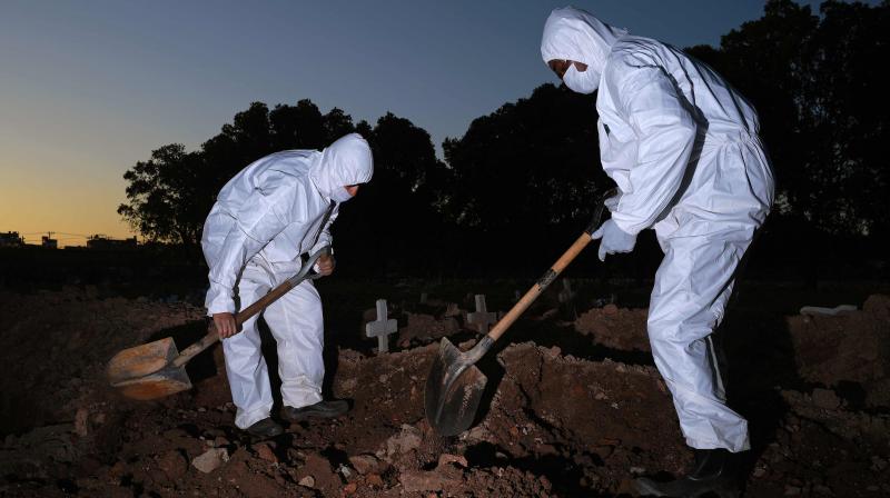 Cemetery workers wearing protective clothing bury a victim of COVID-19 at the Sao Franciso Xavier cemetery in Rio de Janeiro, Brazil. (AFP)