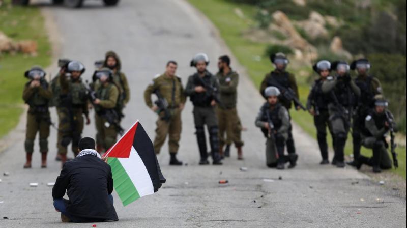 A Palestinian demonstrator holds national flag in front of Israeli forces as they protest against President Donald Trumps Mideast initiative, in Jordan Valley in the West Bank. (AP)