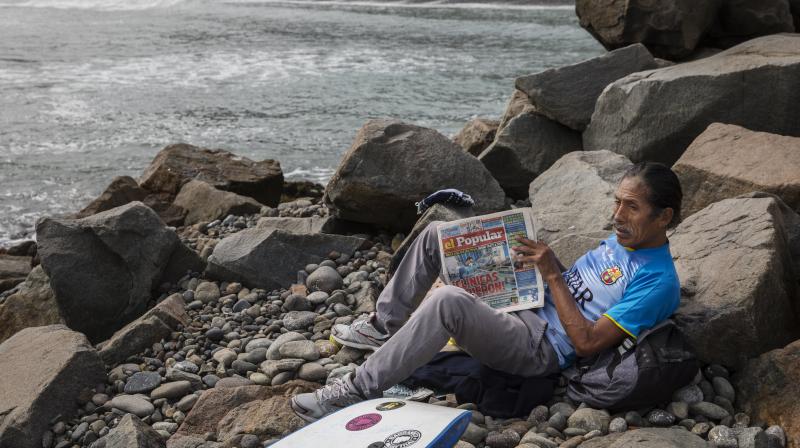 A man reads a newspaper next to the Pacific Ocean on the coast of Lima, Peru. (AP)