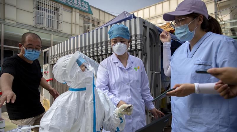 A worker wearing a protective suit talks with people registering for coronavirus tests at a community health clinic in Beijing, Sunday, June 28, 2020.(AP)