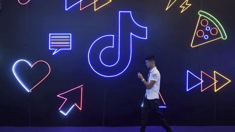 A man uses his smartphone as he walks past a display for Douyin, the Chinese version of video-sharing app TikTok, at an expo in Hangzhou in eastern Chinas Zhejiang Province, Oct. 18, 2019. US president Donald Trump on Thursday, Aug. 6, 2020, ordered a sweeping but unspecified ban on dealings with the Chinese owners of consumer apps TikTok and WeChat, although it remains unclear if he has the legal authority to actually ban the apps from the U.S. (AP)