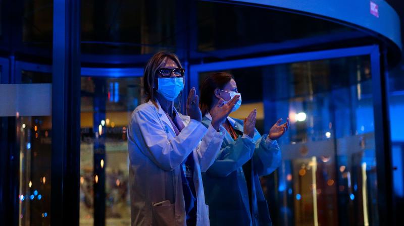 Two healthcare workers dealing with the new coronavirus crisis applaud in return as they are cheered on by members of the Catalan regional police force Mossos dEsquadra, local police officers and other security forces outside the Bellvitge hospital near Barcelona. AFP Photo