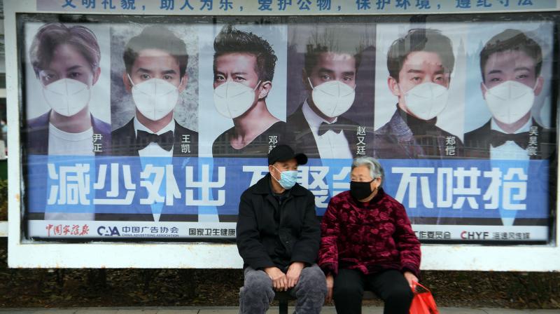 A man and woman sit in front of a poster reminding citizens to wear face masks as a preventive measure against the COVID-19 coronavirus, at a bus stop in Bozhou, in Chinas eastern Anhui province. AFP Photo