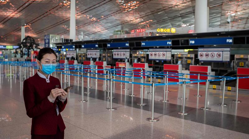 An airline hostess wearing a facemask amid the concerns over the COVID-19 coronavirus holds her smart phone next to empty check-in counters (R) at Beijing Capital International Airport. AFP photo
