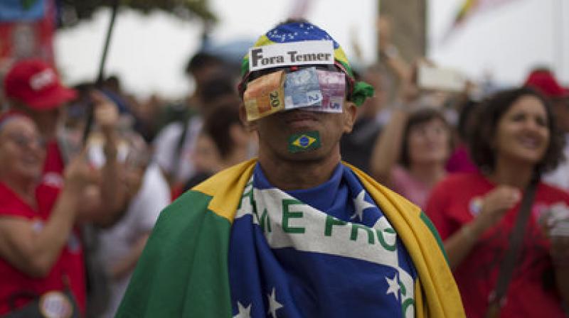 A man poses for the photo with his face covered with money and by a sign that reads in Portuguese 'Temer Out'. (Photo: AP) A man poses for the photo with his face covered with money and by a sign that reads in Portuguese 'Temer Out'. (Photo: AP)