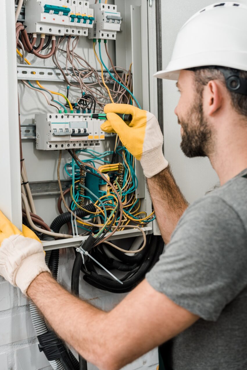 side view of electrician repairing electrical box and using screwdriver in corridor 1