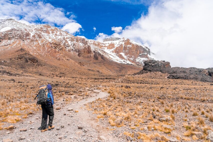 horizontal shot hiker with backpack hiking dry field surrounded by rocks mountains 2