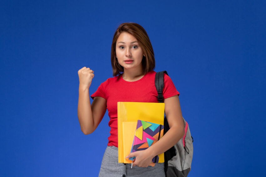 front view young female student red shirt wearing backpack holding files copybook rejoicing blue background 2 1