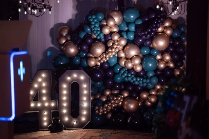 40th birthday celebration backdrop with illuminated marquee numbers and a colorful balloon arrangement in teal gold and purple designed for luxury event decor 1